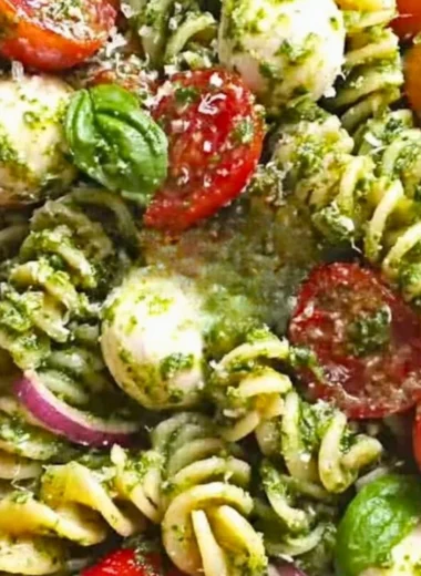 Pesto pasta salad featuring tomatoes and mozzarella, garnished with basil.