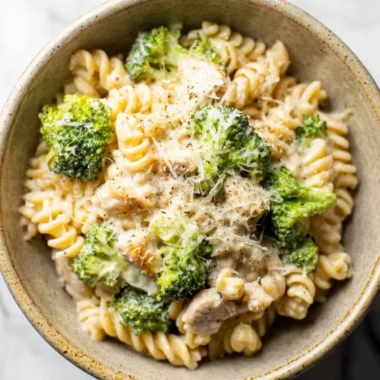 A vibrant bowl of Chicken Broccoli Pasta garnished with fresh herbs and parmesan cheese.