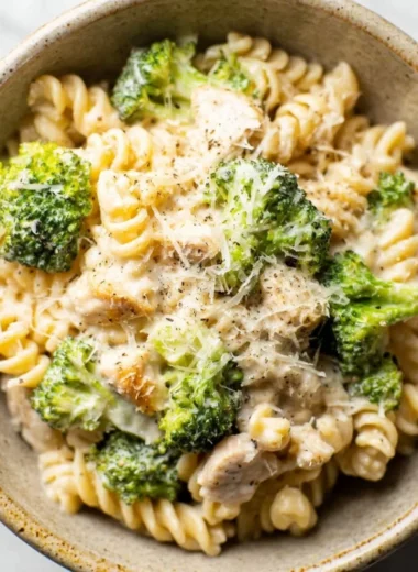 A vibrant bowl of Chicken Broccoli Pasta garnished with fresh herbs and parmesan cheese.