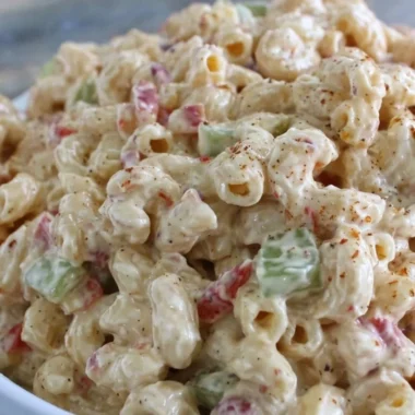 Creamy macaroni salad served in a bowl with fresh vegetables and herbs