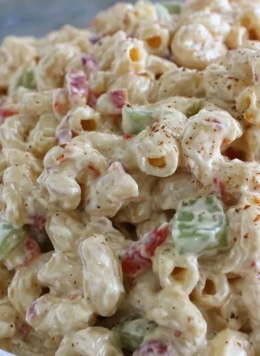 Creamy macaroni salad served in a bowl with fresh vegetables and herbs