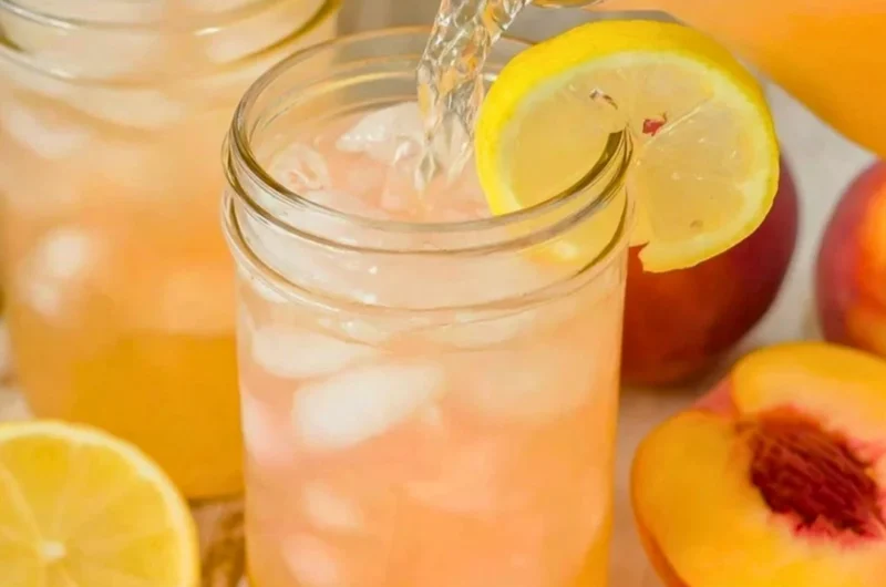 Glass of homemade peach lemonade with fresh peaches and lemons