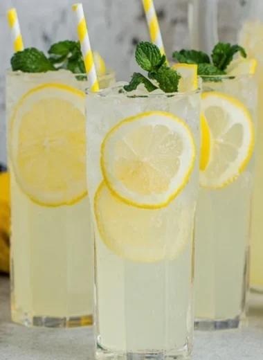 A glass of old-fashioned homemade lemonade with fresh lemons and mint.