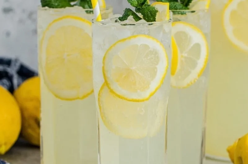 A glass of old-fashioned homemade lemonade with fresh lemons and mint.