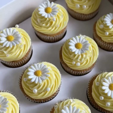 Pastel yellow cupcakes decorated with daisies and pearls for a beautiful presentation.