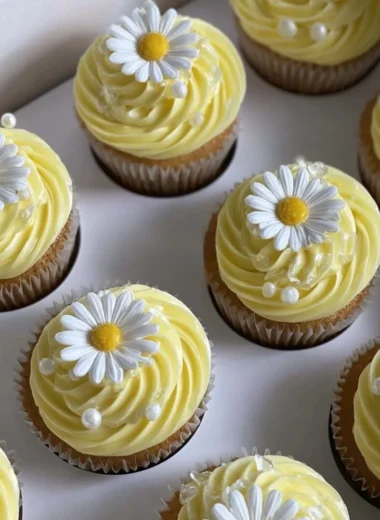 Pastel yellow cupcakes decorated with daisies and pearls for a beautiful presentation.