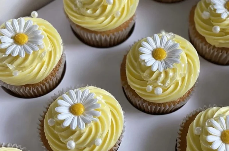 Pastel yellow cupcakes decorated with daisies and pearls for a beautiful presentation.
