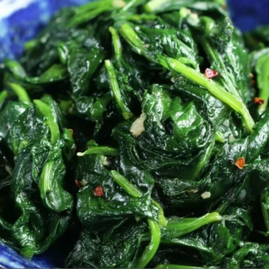 A plate of quick and easy sautéed spinach garnished with garlic and lemon.