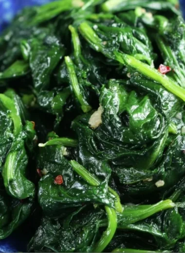 A plate of quick and easy sautéed spinach garnished with garlic and lemon.