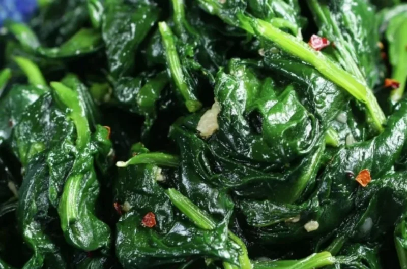A plate of quick and easy sautéed spinach garnished with garlic and lemon.
