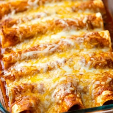 Plate of restaurant-style red cheese enchiladas topped with cheese and fresh herbs