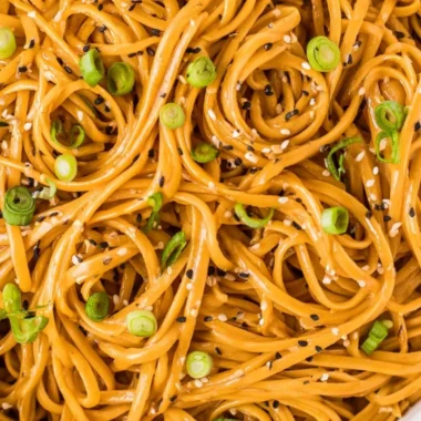 Bowl of savory sesame noodles topped with fresh vegetables and sesame seeds