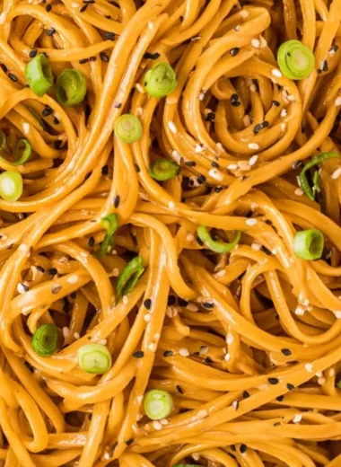 Bowl of savory sesame noodles topped with fresh vegetables and sesame seeds
